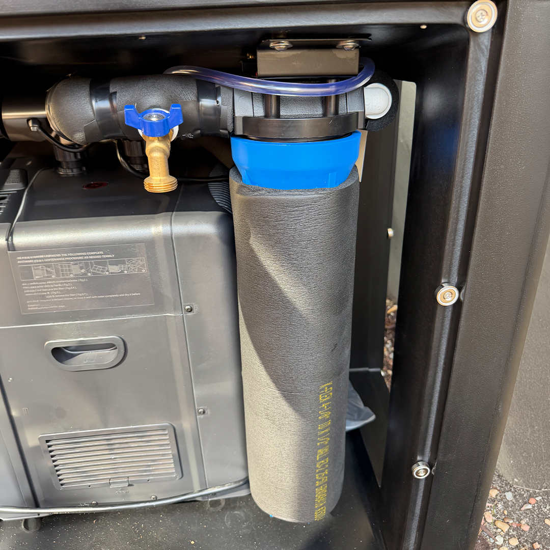 A close-up of a water filter system component mounted inside a black metal housing, featuring a gray cylindrical filter with yellow text, a bright blue top section, and a black connector with a blue valve.