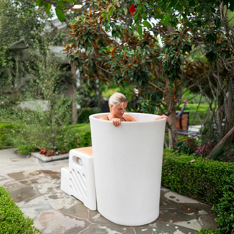 A woman sitting in a white vertical tub surrounded by greenery