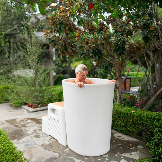 A woman sitting in a white vertical tub surrounded by greenery